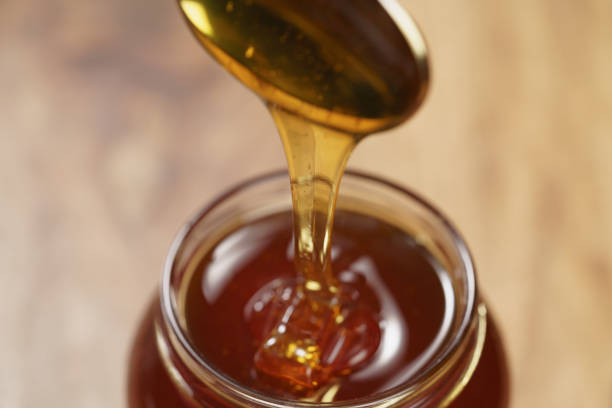 istock pouring organic honey from spoon into glass jar 1496853944