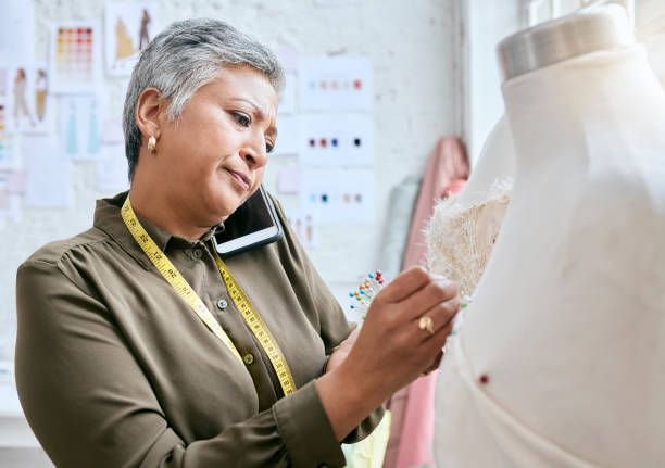 istock Phone call, textile and senior woman with tailor, design process and fabric communication for client or business. Smartphone, boss, fashion designer or person working on mannequin in workshop studio 1496857101