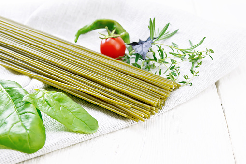 Spinach spaghetti, tomatoes, basil, rosemary and pepper, spinach leaves on a napkin on wooden board background