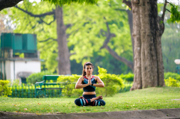 kobieta siedząca w pozycji lotosu wykonuje gest namaste , ćwicząc jogę i medytując na świeżym powietrzu w parku - zen like nature breathing exercise sitting zdjęcia i obrazy z banku zdjęć