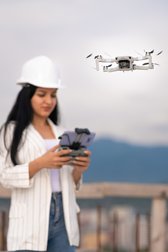 Close-up of a drone operated by a beautiful young female engineer-surveyor in a white helmet on a construction site. Architectural Engineer and Safety Inspector. Vertical photo