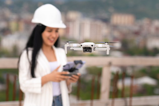 Close-up of a drone operated by a beautiful young female engineer-surveyor in a white helmet on a construction site. Architectural Engineer and Safety Inspector