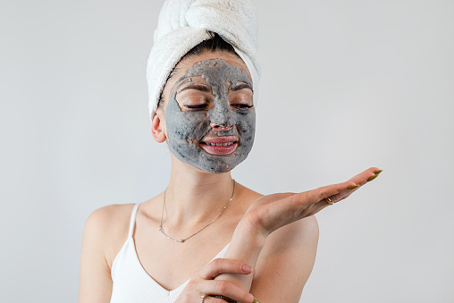 Beautiful young woman with a black mud or clay mask for the face isolated on white. Skin care anti aging beauty treatment