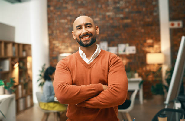 Face, arms crossed and happy businessman in coworking space at night with pride for creative startup. Smile, portrait or confident male designer working late in modern office on deadline project stock photo
