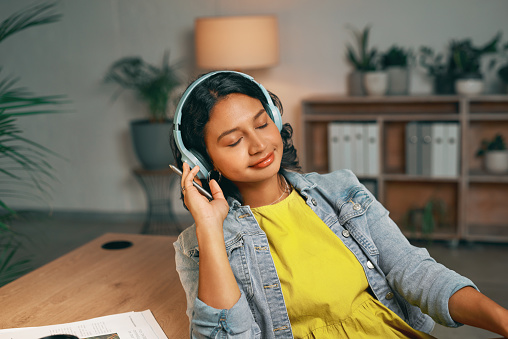 Smile, headphones and student listening to music in house living room for late night study break, relax or rest. Happy, woman and Indian person streaming song, radio or podcast for study help at home