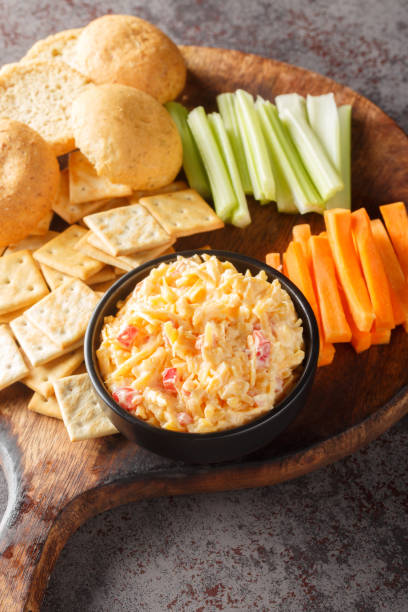 istock Pimento cheese is a versatile, creamy dip served with vegetables and crackers closeup on the wooden board on the table. Vertical 1496870144