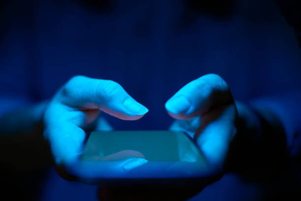 Primo piano della donna che utilizza il telefono cellulare con effetto di illuminazione blu - foto stock