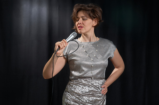 Half-length portrait of a singing woman with a microphone on a black background