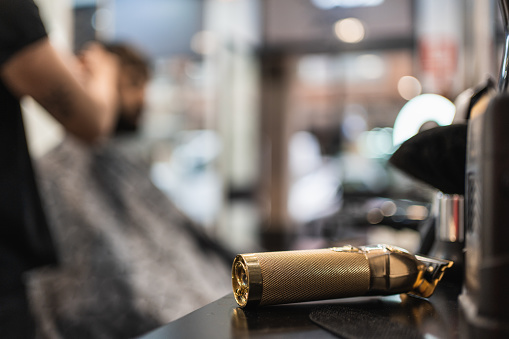 Close-up image of a gourmet golden hair clipper resting on a barbershop shelf while someone is getting a haircut.