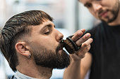 Barber combing and grooming his client's mustache with a small round brush in the barber shop.