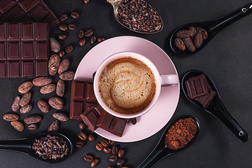 Aromatic cappuccino coffee cup with cafe beans, chocolate bar, cacao nibs on black background