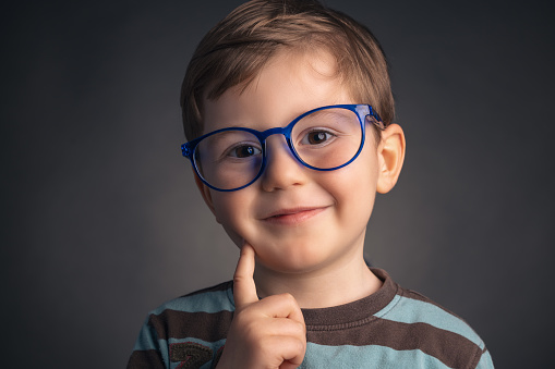 Cute, smile, funny and clever, little boy with glasses, studio portrait on black background. Smart preschooler.