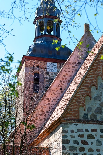 A historical church building featuring a tall tower with a clock face at the top in lush greenery