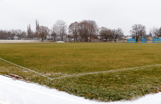 Review of sports stadium. A large football field covered with grass, with gates, markings and stands for referees. Outdoors, winter