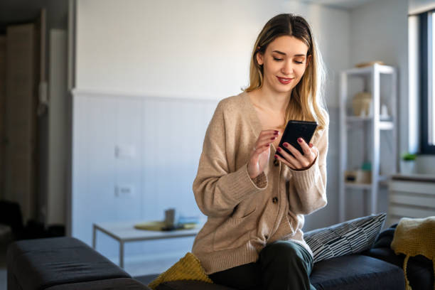 istock Young woman wearing sweater using smartphone at home, communication and social network concept, 1496876288
