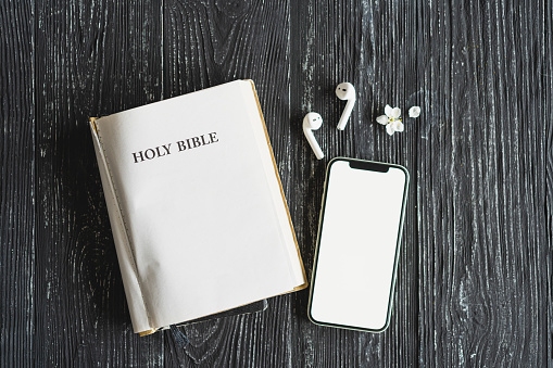 Study Bible worship online concept. Church online Sunday new normal concept. Bible, cell phone and earbuds on a wood background. Home church