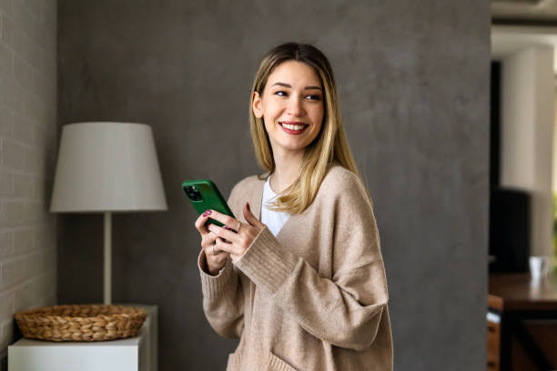 istock Young woman wearing sweater using smartphone at home, communication and social network concept, 1496877938
