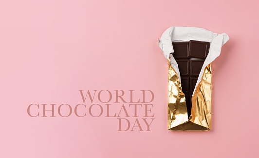 World Chocolate Day, july 07.  Dark chocolate bar pieces with nuts on pink background, top view, copy space. Holiday greeting card or banner concept.