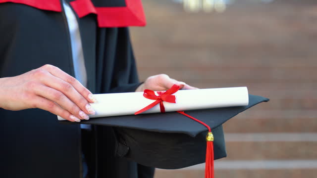 Hand of student girl holding diploma and graduation cap in commencement day, concept of successful education