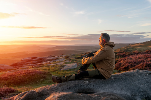 Bearded  Man in orange jacket relaxing alone on the top of  mountain  and drinking hot coffee at sunrise. Travel  Lifestyle concept The national park Peak District in England