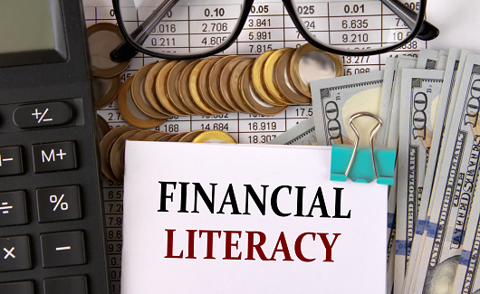 FINANCIAL LITERACY - words on a white piece of paper on the background of a calculator, pennies and glasses
