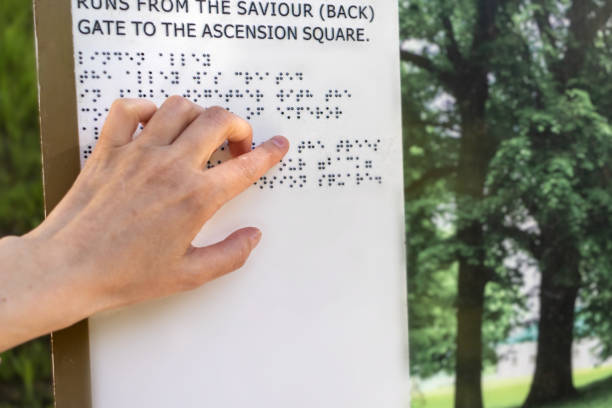 una mujer ciega lee un letrero con braille en un recorrido por un parque de verano. primer plano de la mano. asistencia a las personas con discapacidad visual - outdoors book reading accessibility fotografías e imágenes de stock