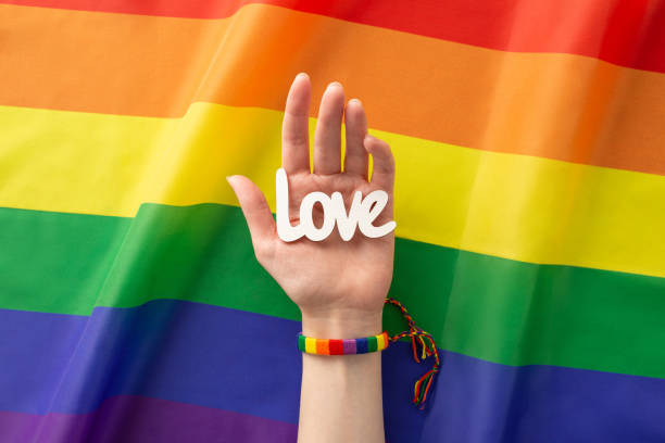 A first person top-down view of a woman's hand sporting a rainbow bracelet and holding the word una vista en primera persona de arriba hacia abajo de la mano de una mujer luciendo un brazalete de arco iris y sosteniendo la palabra