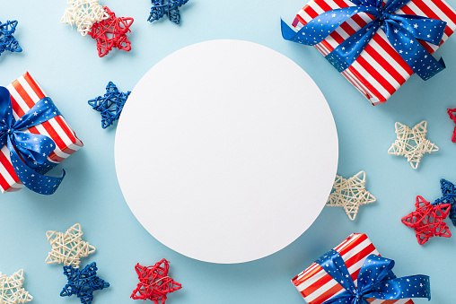 Patriotic theme for Independence Day. Top view of party accessories: rattan stars and gift boxes in symbolic wrapping, on a blue background with an empty circle for text or advertising