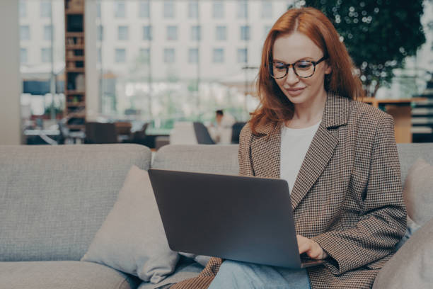 istock Woman working remotely in coworking space, using laptop while sitting on couch 1496892861