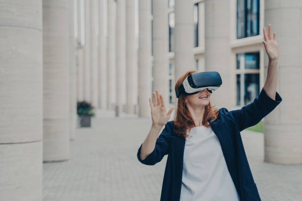 istock Young ginger woman dressed formally stands outdoors and using VR headset 1496892884