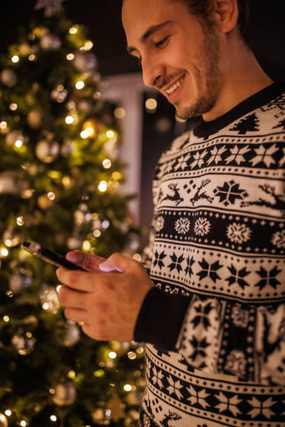 istock Young man standing by the Christmas tree, using smart phone 1496893378
