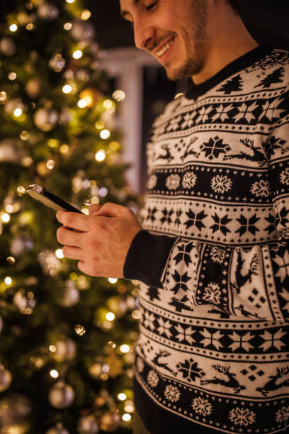 istock Young man standing by the Christmas tree, using smart phone 1496893412