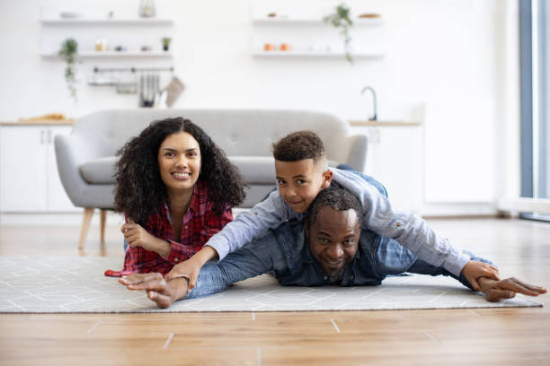 vater hält sohn auf dem rücken, während er mit mama auf dem boden bleibt - couple loving lying on back carpet stock-fotos und bilder