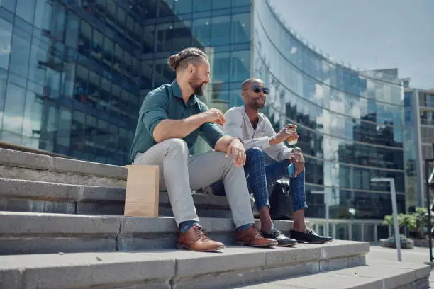 Photo of City, steps and men sitting on lunch break to relax with coffee, sun and smile with work friendship. Talking, relaxing at meal time and startup employees on stairs outside office building together.