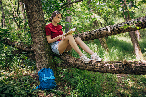 Young woman reading a book in the forest and enjoying nature