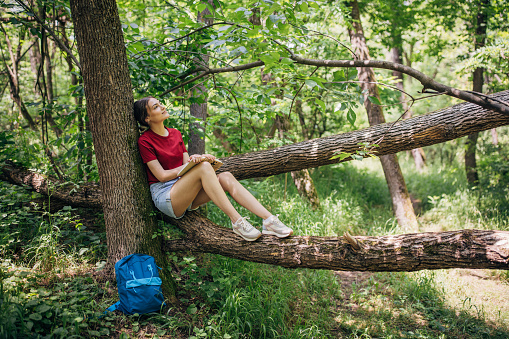 Young woman reading a book in the forest and enjoying nature