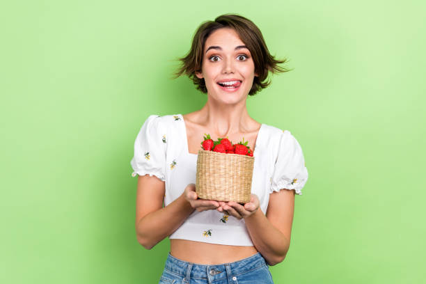 foto de dulce mujer complicada vestida blusa blanca recogiendo bayas maduras aislado color verde fondo - tasting women eating expressing positivity fotografías e imágenes de stock