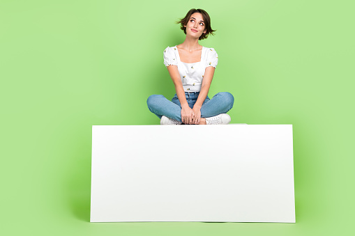 Full length photo of shiny dreamy lady wear white blouse sitting modern gadget looking empty space isolated green color background.