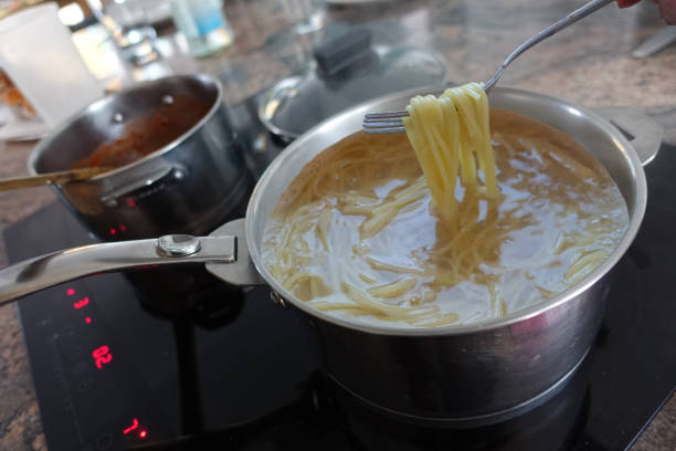 istock Spaghetti in boiling water and tomato sauce being cooked on a ceramic hob 1496899649
