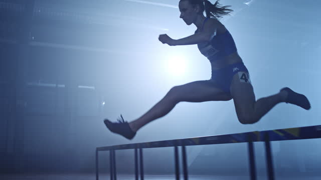 SLO MO TS Female sprinter jumping hurdles in a competition at night