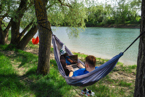 istock A young man works on his laptop while lying in a hammock on the river bank 1496904541