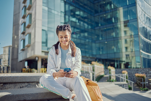 Technology, woman on her smartphone and by a building outdoors in a city with smile. Social networking or online communication, connectivity and female person on her cellphone typing or writing