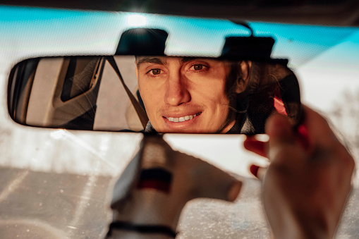 A smiling man adjusts the rearview mirror of the car