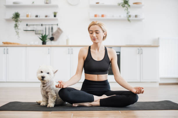 istock Blonde peering at dog while sitting in lotus position on mat 1496906425