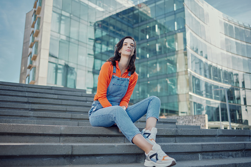 Buildings, fashion and woman thinking on steps or sitting on stairs in a city and in street style or clothing. Summer, travel and female person or model in urban clothes outdoor in a town