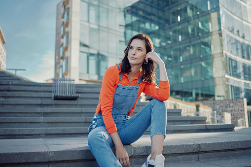 Buildings, fashion and woman relax on stairs or sitting on steps in a city thinking of street style or clothing. Summer, travel and female person or model in urban clothes outdoor in a town