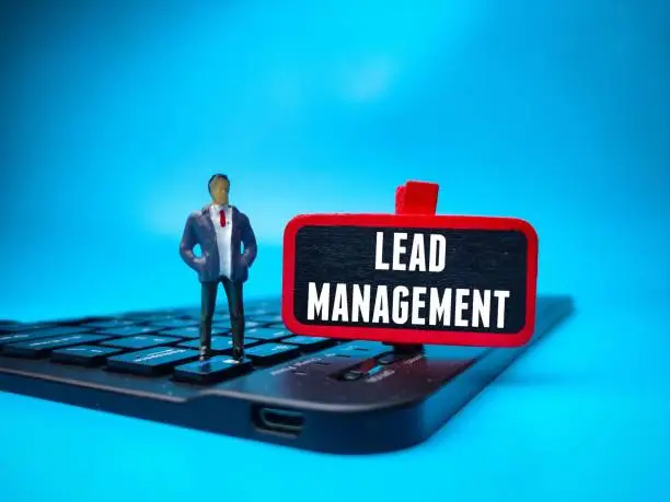 A person in a miniature figurine standing on a keyboard with a sign that says 'Lead Management'