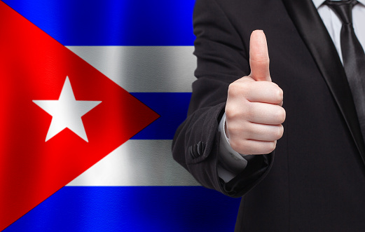 Cuban concept. Businessman showing thumb up on the background of flag of Cuba