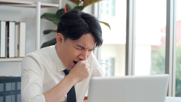 istock Exhausted young asian worker yawning at workplace. Business man using laptop for working feeling sleepy and yawning tired from overwork job 1496910247