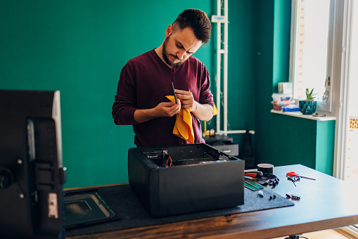 A focused millennial man repairs a computer at home, wipes the SSD HDD with a cloth